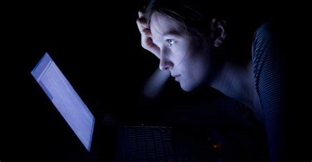 Woman in a dark room looking at bright computer screen